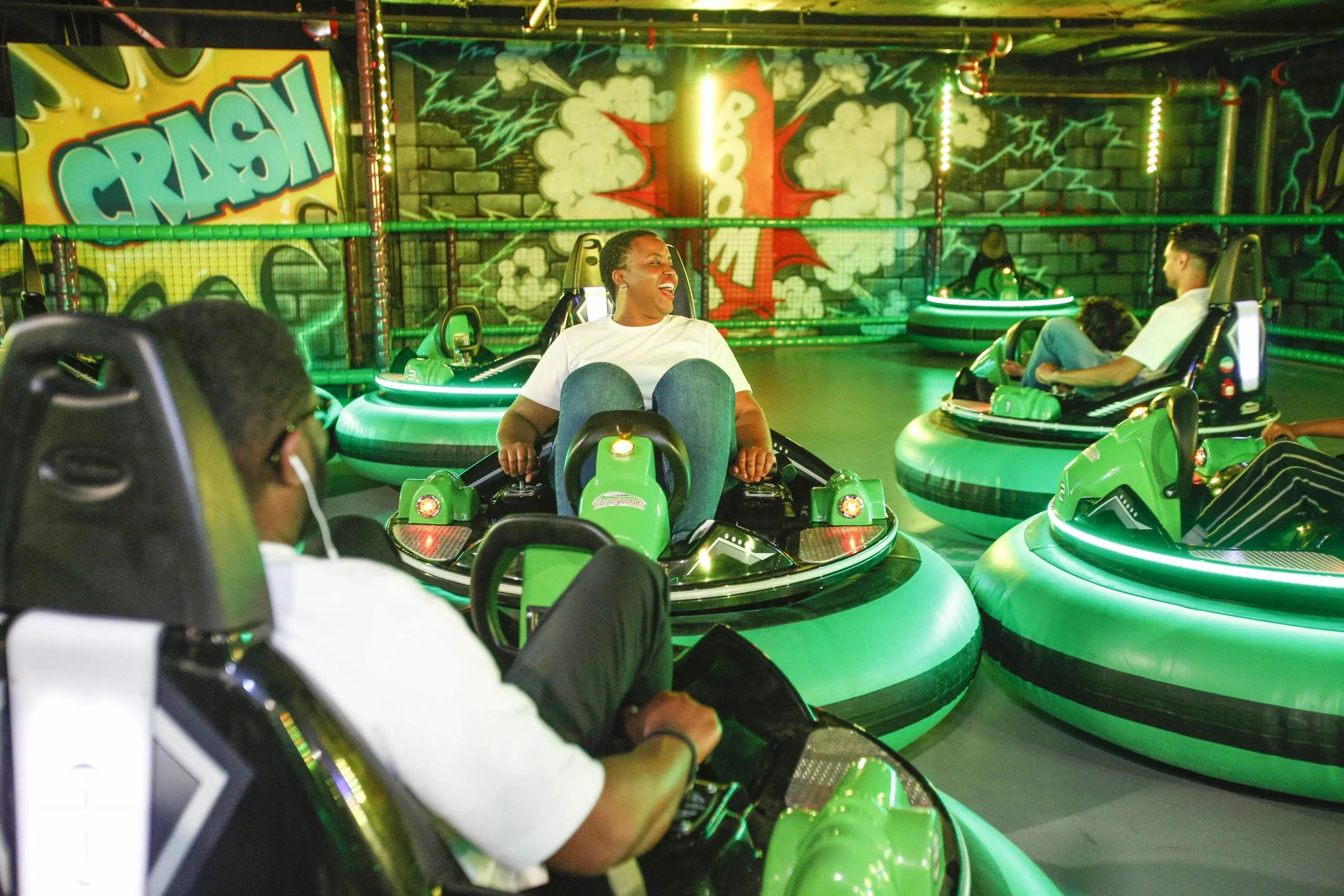 Indoor bumper car arena with bright green cars and colourful graffiti-style wall art featuring words like ‘Crash’ and ‘Boom.