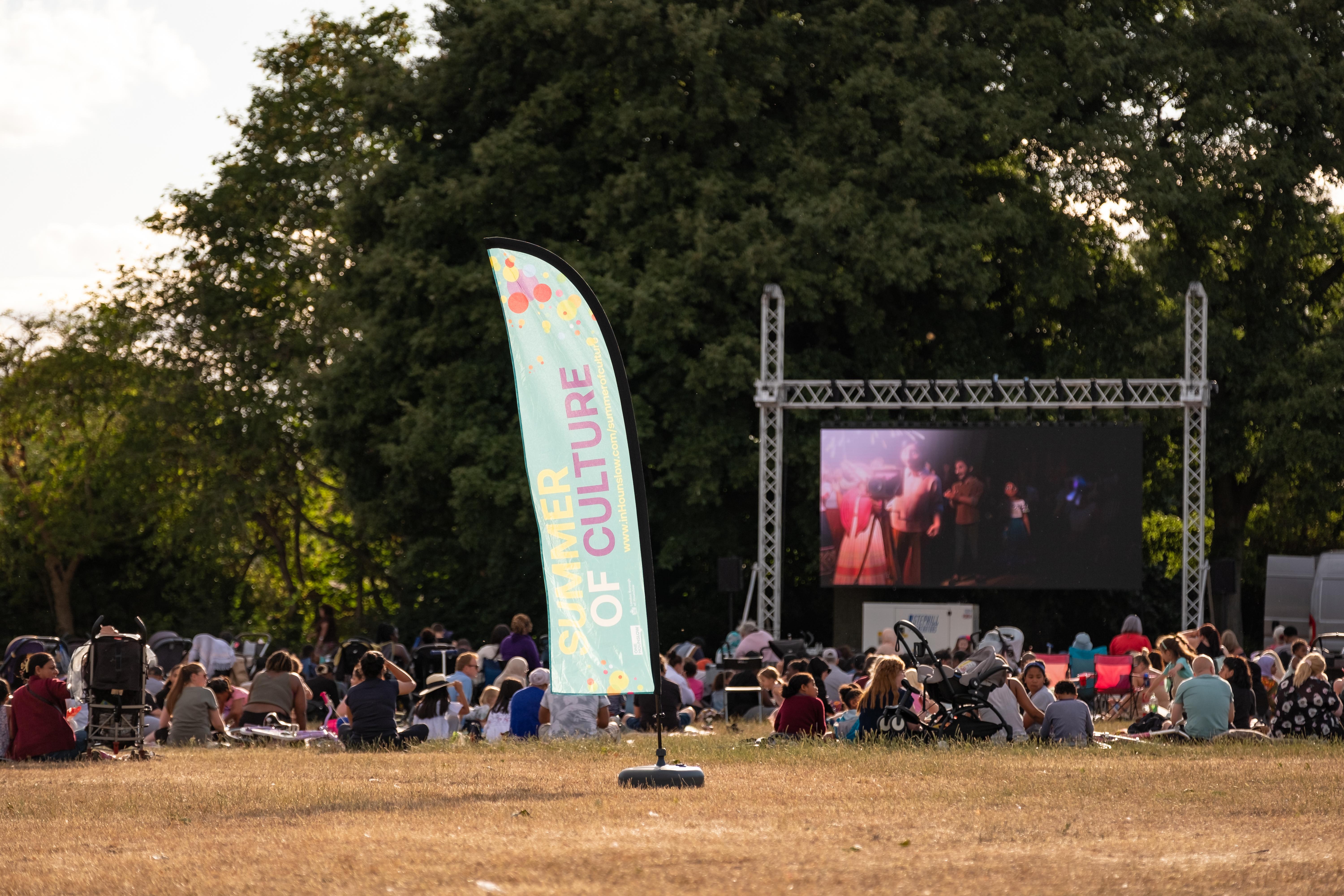 A movie being played on a large screen in a local park in Hounslow as part of films on the green.