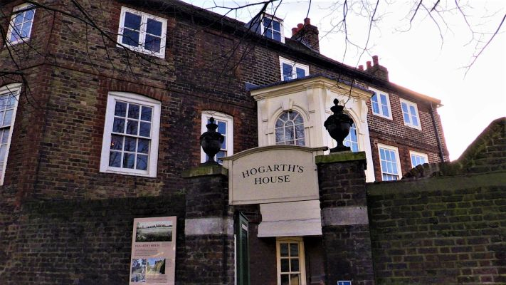 Historic brick building with a sign reading ‘Hogarth’s House’ above the entrance, seen behind a stone wall and gate.